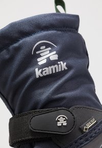 Marineblaue Textil-Schneestiefel mit schwarzem Riemenverschluss und Logo. Verfügt über eine strukturierte Oberfläche und eine grüne Schlaufe. Ausgestattet mit Gore-Tex.