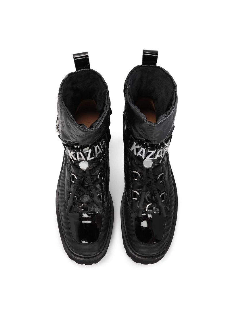 Stivali neri alla caviglia realizzati in materiale lucido con colletto imbottito, dotati di lacci, hardware in argento e il nome del marchio "KAZAR" sulla parte frontale.