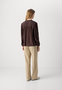 Brun silkebluse med samlet detalje bagpå, parret med beige skræddersyede bukser. Glat stof med lange ærmer og subtil glans.
