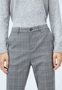 Szare spodnie w kratę z subtelnym wzorem. Posiadają zapięcie na guzik, boczne kieszenie oraz dopasowany krój. Wykonane z lekkiego materiału.