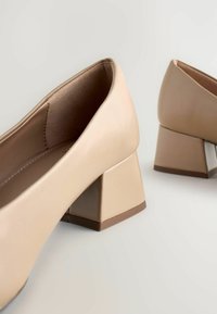 Pantofi bej cu toc bloc, exterior din piele netedă, vârf pătrat și design cu toc jos și lat. Interiorul are o căptușeală moale.