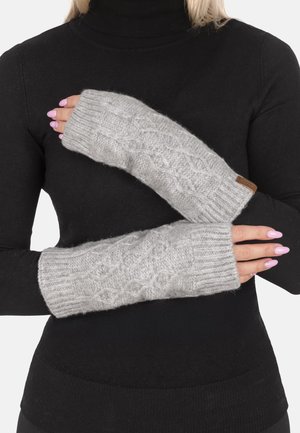 Grijze gebreide vingerloze handschoenen met kabelpatroon, gedragen op gekruiste armen over een zwarte coltrui.