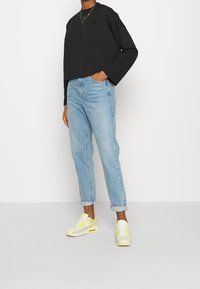 Svart kortärmad långärmad skjorta, ljusblå högmidjade jeans och vita sneakers med gula accenter. Enkel design, bekväm passform.