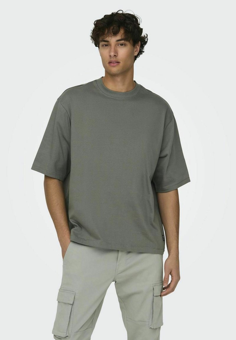 T-shirt gris oversize en tissu doux et lisse; encolure ronde; manches courtes; associé à un pantalon cargo clair avec poches latérales.