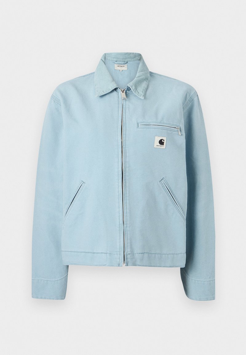 Veste à fermeture éclair bleu clair avec col, deux poches latérales et une poche poitrine zippée ornée d'un petit patch logo noir et blanc.