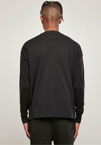 Svart långärmad sweatshirt med rund halsringning, texturerad tyg och ribbade cuffar. Har en avslappnad passform och en förlängd bakslut.