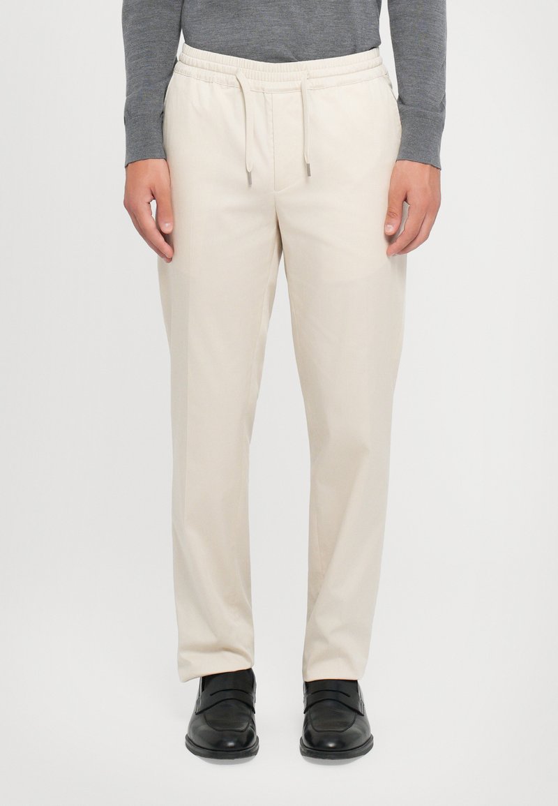 Pantaloni bej cu bandă elastică la talie și sfoară. Material neted și picioare înguste. Purtați cu pantofi negri, evidențiind un aspect casual, dar rafinat.