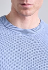 Light blue knit sweater with a textured, breathable pattern and ribbed round neckline. Close-up view focuses on neckline area.