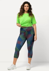 Groene sport T-shirt met korte mouwen, gecombineerd met gestreepte capri leggings in blauw, groen en bordeauxrood. Witte sneakers maken de outfit compleet.