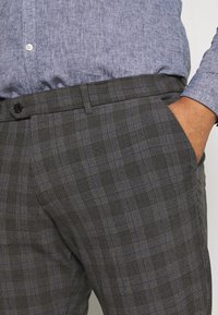 Grijze geruite broek met contrasterende blauwe lijnen, een gladde textuur, zijzakken en een zwarte knoopsluiting bij de tailleband.