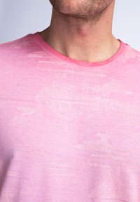 Camiseta rosa de tela suave y texturizada con un sutil patrón de formas abstractas. Diseño de cuello redondo con un cuello liso.
