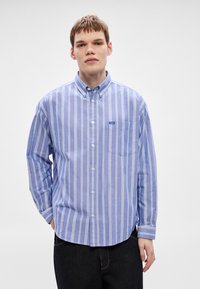 Hellblau gestreiftes Hemd mit weißen Streifen, mit Brusttasche und kleinem Markenlabel, aus einem gewebten Stoff gefertigt.