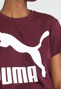 Burgundy T-shirt made from cotton, featuring a large white Puma logo and bold text in white. Short sleeves and round neckline.
