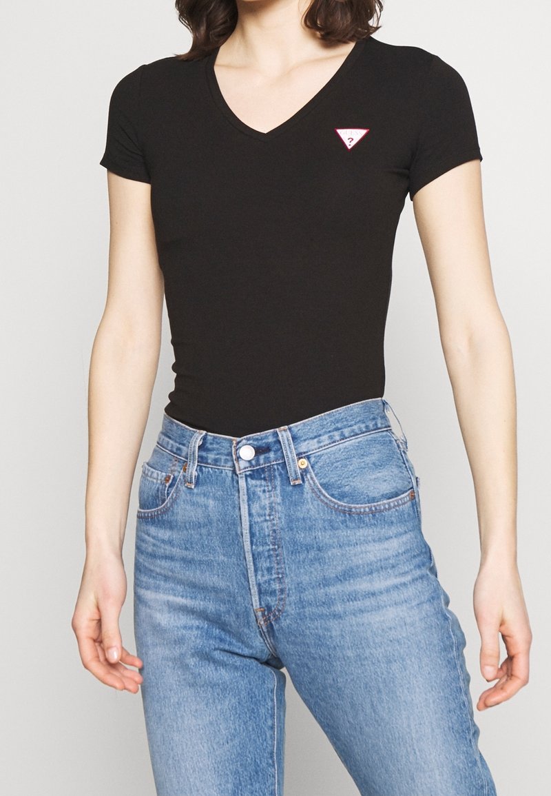 T-shirt noir à manches courtes et col en V avec un petit logo triangulaire rouge sur la poitrine gauche, associé à un jean en denim bleu taille haute.