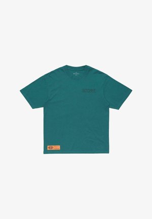 T-shirt à manches courtes bleu sarcelle avec un petit texte noir sur le côté gauche de la poitrine et un patch rectangulaire orange près de l'ourlet inférieur à l'avant.