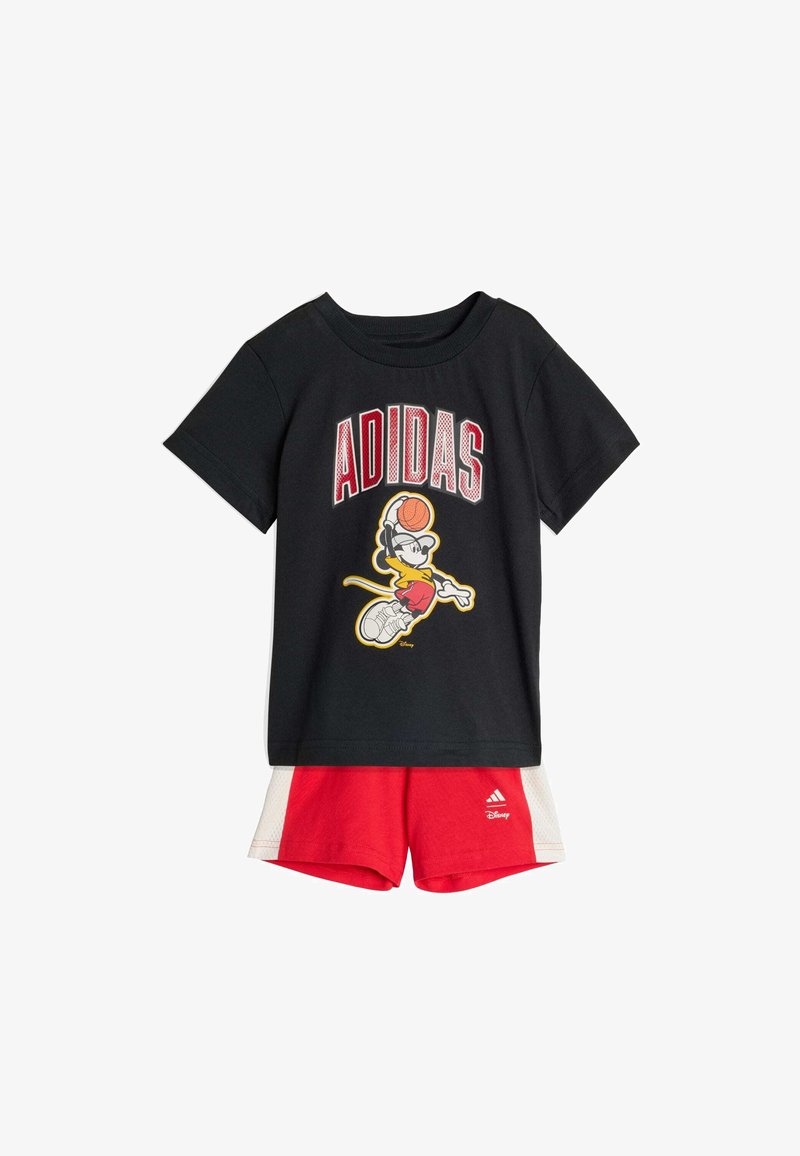 Camiseta de algodón negra con un gráfico de un personaje jugando baloncesto, combinada con pantalones cortos de malla rojos y blancos con el logo de Adidas.