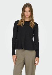 Musta, pitkähihaisen yläosa, jossa istuva vartalo ja levenevä helma. Pehmeä pinta, pyöreä pääntie, yhdistetty vaaleisiin housuihin.