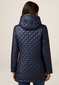 Chaquetón acolchado de color azul marino con capucha, que presenta una textura suave y brillante y un patrón de rombos, extendiéndose hasta la mitad del muslo.