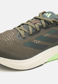 Baskets de course avec une tige en mesh olive respirant, des accents noirs et une semelle blanche rembourrée avec des détails verts.