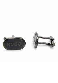 Polsini in metallo nero a forma ovale con logo "HUGO" in rilievo. Texture liscia con finitura lucida e design slanciato.