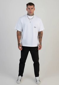 Biały bawełniany t-shirt z krótkimi rękawami i haftowanym logo; zestawiony z czarnymi spodniami z przetarciami, wytartymi miejscami i kieszeniami.