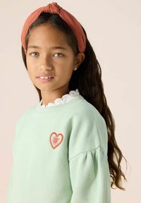 Sweatshirt vert menthe avec des manches bouffantes, arborant une broderie de cœurs rouges et roses. Accompagné d'un bandeau texturé couleur rouille.