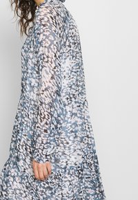 Tiskované maxi šaty s modrou základnou a abstraktními vzory v růžové a černé barvě, dlouhými rukávy a vrstveným designem sukně.