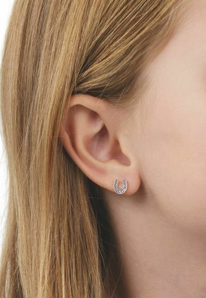 Kleiner silberner hufeisenförmiger Ohrring mit eingebetteten Steinen, getragen am linken Ohr einer Person mit glattem, blondem Haar.