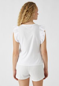 Witte katoenen tanktop met ruches op de mouwen, gecombineerd met getextureerde witte shorts. Glad materiaal en een ontspannen pasvorm, achterzijde zichtbaar.
