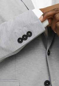 Light gray suit jacket with a smooth texture, featuring a black button closure on the cuff and subtle stitching details.