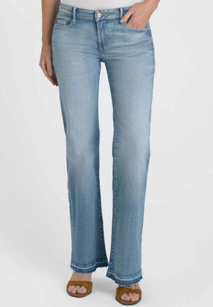 Light blue straight-leg jeans with frayed hems worn by a person with one hand in pocket and brown open-toe sandals.