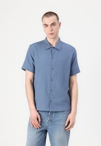 Short-sleeve, button-up shirt in light blue textured fabric, featuring a collar and a regular fit, paired with faded blue jeans.