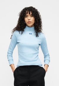 Γαλάζιο ριμπ ζιβάγκο με μακριά μανίκια και μικρό μπλε λογότυπο Hugo στο στήθος, σε συνδυασμό με μαύρο παντελόνι.