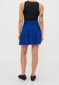 Haut sans manches noir associé à une jupe en dentelle bleue avec un ourlet à volants. La jupe comporte une taille smockée et des motifs ajourés complexes.