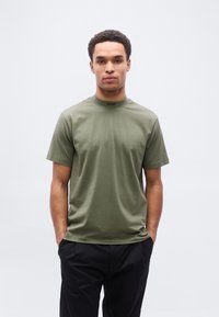 Λαδί βαμβακερό T-shirt με στρογγυλή λαιμόκοψη, κοντά μανίκια και μικρό μαύρο λογότυπο "BOSS" στον γιακά. Λείος υφής, άνετη εφαρμογή.