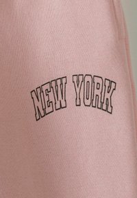Roze sweatshirt van een zachte, gewaxt stof. Heeft een zwarte "NEW YORK" print in een vetgedrukt, gebogen lettertype over de borst.