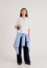 Balta saīsināta t-krekls, gaiši zila svītrainā krekls sasieta ap vidukli, tumšas platām kāju biksēm, sudraba ķēdes kaklarota un maza somiņa.