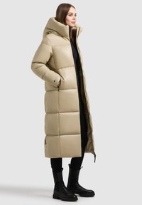 Abrigo puffer beige con cuello alto y diseño acolchado horizontal. Cuenta con bolsillos laterales y cierre de cremallera, combinado con botas negras.