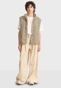 Västar i leopardmönster, beige med dragkedja fram, ihop med krämfärgade oversized plisserade byxor och ljusa sneakers.