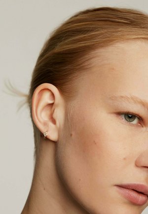 Pendiente de oro con un diseño floral, decorado con pequeñas piedras blancas. Vista de cerca que destaca los intrincados detalles.