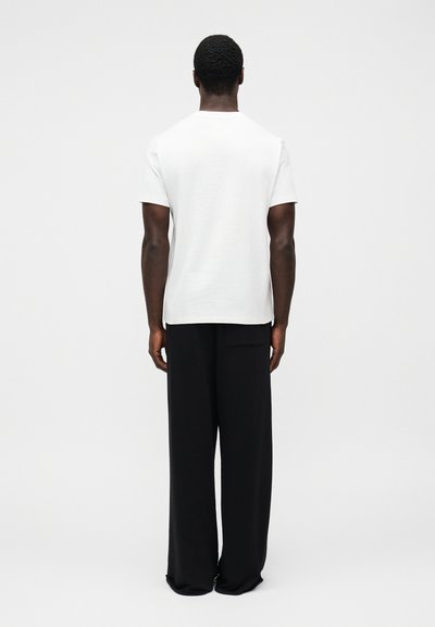 Λευκό κοντομάνικο t-shirt συνδυασμένο με φαρδιά μαύρη παντελόνια, ομαλή υφή, απλός σχεδιασμός, και λεπτομέρεια με πίσω τσέπη στην παντελόνα.