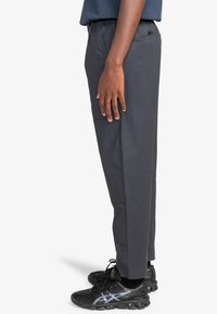 Donkergrijze, lichte, elastische broeken met een comfortabele pasvorm; met een zijzak en verstevigde stiksels, gecombineerd met zwarte sportschoenen.