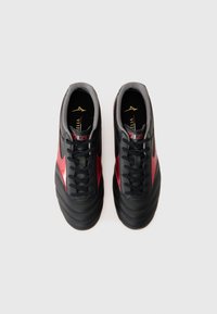 Black and red soccer shoes with a smooth leather upper, textured accents, lace-up design, and cushioned interior. Gold logo on insole.