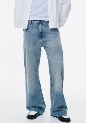 Jeans in denim blu chiaro con vestibilità rilassata, caratterizzati da una trama sbiadita, design a cinque tasche e cuciture in contrasto. Abbinati a scarpe nere.