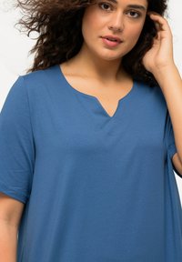 Top blu con scollo a V e maniche corte, realizzato in tessuto morbido. Presenta una vestibilità rilassata e dettagli di cucitura discreti sullo scollo.