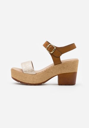 Sandale compensée marron et beige avec une bride avant métallique, une bride de cheville réglable avec une boucle dorée et une semelle plateforme texturée.