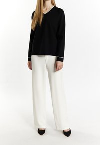 Černý svetr s výstřihem do V a bílým lemem, v kombinaci s volnými bílými kalhotami a černými lodičkami s špičatou špičkou. Hladká tkanina a uvolněný střih.