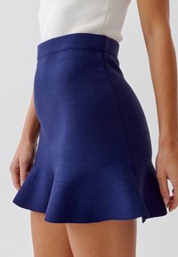Námořnickomodrá pletená sukně s rozšířeným spodním lemem a hladkým pasem, zvýrazněná jemnými švy.