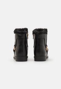 Bottines noires avec garniture en fourrure synthétique, finition en cuir lisse, fermetures éclair sur le côté et un petit talon carré. Accentuées par des éléments en métal doré.