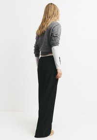 Šedý strihaný sveter s rebrovanou textúrou cez biele tričko s dlhým rukávom, skombinovaný s čiernymi nohavicami s širokými nohavicami. Mäkké, neutrálnych odtieňov obuv.